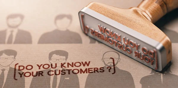 A rubber stamp marking the words “Do you know your customers?” onto paper, symbolizing the KYC onboarding process