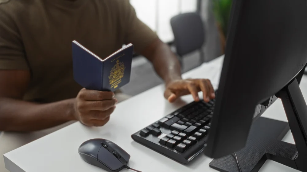 User holding passport while entering information on a computer during online identity verification, representing automated KYC document validation