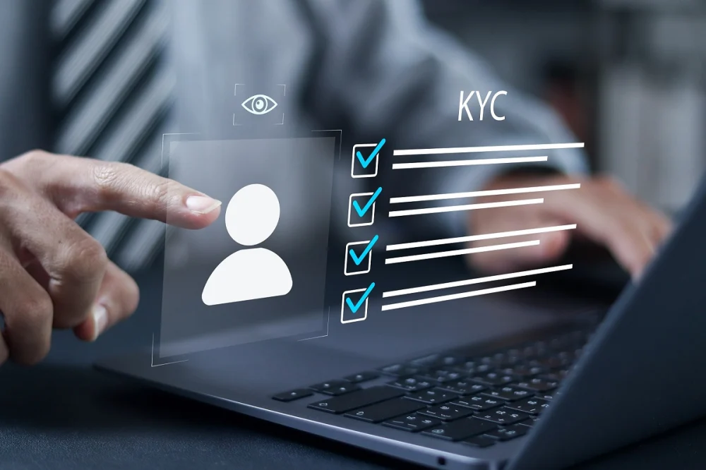 Hand pointing to a digital KYC checklist on a laptop screen, showing identity review and verification tasks